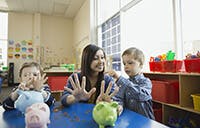 Female teacher with two small children counting on their hands.